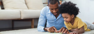 african american father and son lay on the rug in the living room reading a book together