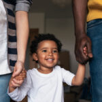 biracial family standing while little boy holds his parents hands